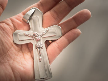 Close-up of hand holding cross against gray background