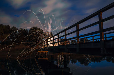 Illuminated bridge over river against sky at night