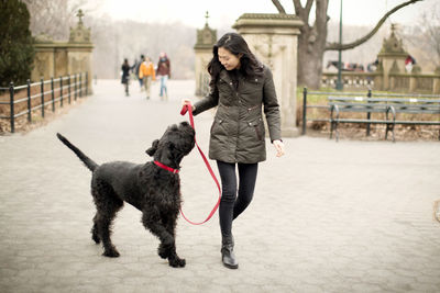 Happy woman looking at dog while walking on footpath