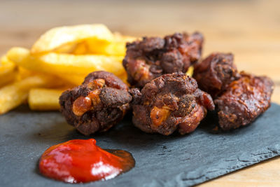 Close-up of fried chicken wings and french fries with ketchup on slate