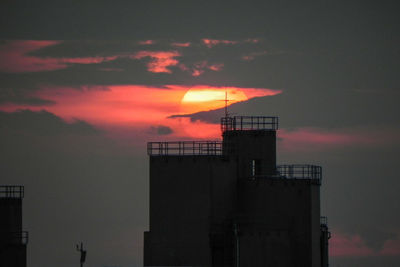 High section of silhouette building against cloudy sky during sunset