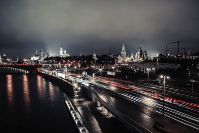 Light trails on river by city against sky at night