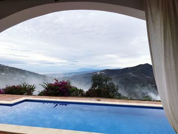 Scenic view of swimming pool against sky seen through window