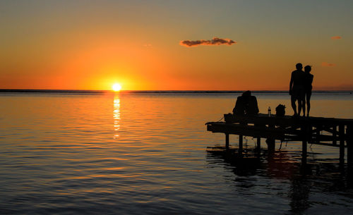 Silhouette couples on pier at sea during sunset