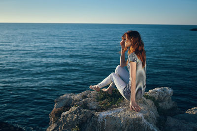 Woman on rock by sea against sky