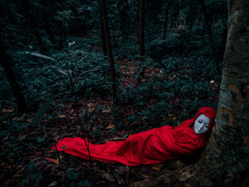 Person wearing mask wrapped in red blanket lying on field