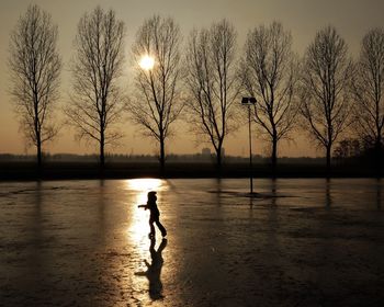 Silhouette boy standing in lake against sky during sunset
