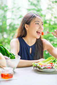 Young woman eating salad on table at home