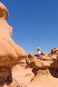 Low angle view of boy standing on rocks against clear blue sky