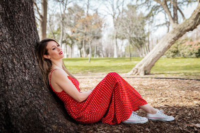 Smiling woman leaning on tree trunk on land 