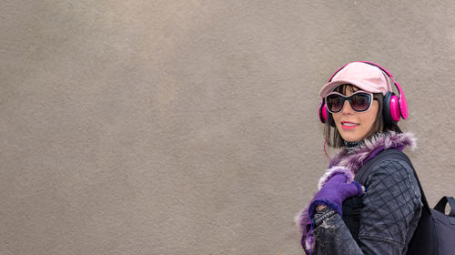 Side view of woman wearing sunglasses and headphones against wall