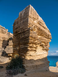 View of rock formation in sea against clear blue sky