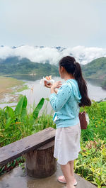 Side view of woman eating while standing and watching the lake leonard