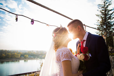 Couple kissing against lake and sky on sunny day