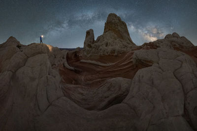 Silhouette of unrecognizable explorer standing with flashlight on scenery of rocky formations in highlands under milky way starry sky in vermillion cliffs national monument, arizona in usa