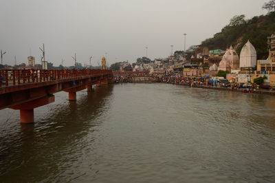 Bridge over river by buildings in city against clear sky