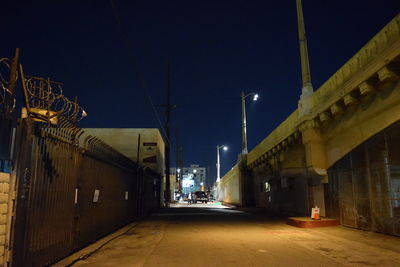 Illuminated road amidst buildings against sky at night