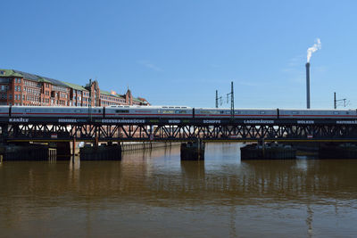 Train on bridge over river against sky in city