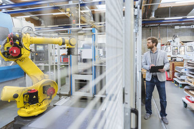 Businessman looking at industrial robot in modern factory