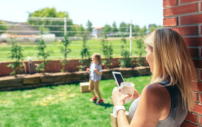 Mother using phone while son playing in lawn