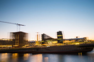 Bridge over river by buildings against clear sky