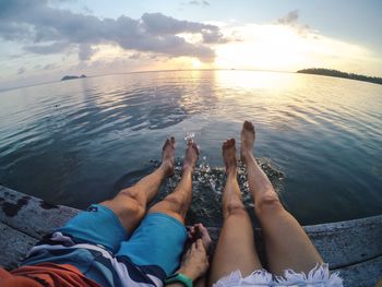 Low section of couple relaxing by sea on pier during sunset