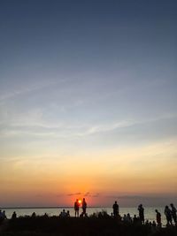 Silhouette people on beach against sky during sunset