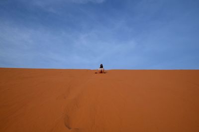 Man on sand dune in desert against sky