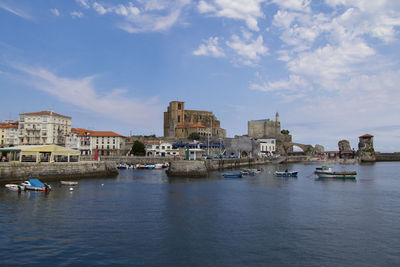 View of buildings by river against cloudy sky