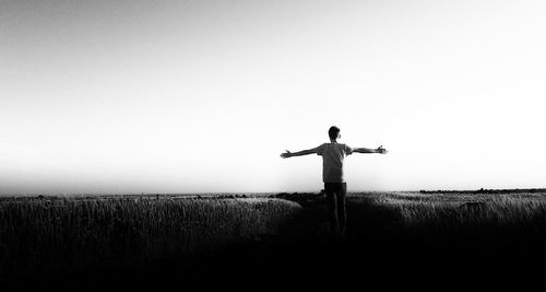 Rear view of boy with arms outstretched standing on field against clear sky