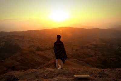 Rear view of man standing on mountain during sunset