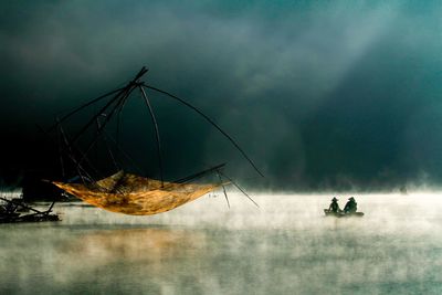 People in boat on lake by fishing net during foggy weather
