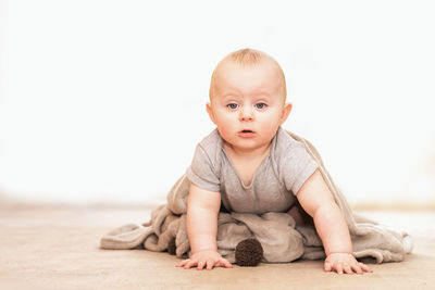 Portrait of cute baby boy on floor against wall at home