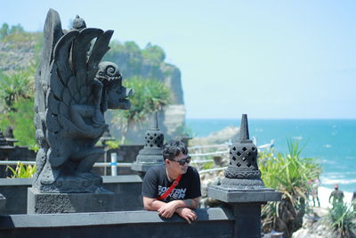 Man sitting by statue against sea