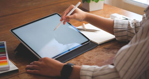 Midsection of woman using digital tablet on table