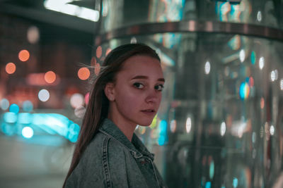 Portrait of young woman against column at night