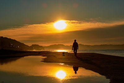 Silhouette man standing on beach against orange sky