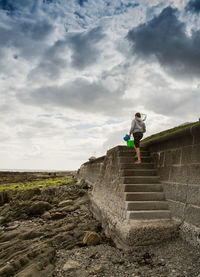 Rear view of boy moving on steps against cloudy sky