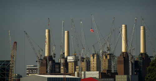 Panoramic view of cranes and buildings against clear sky