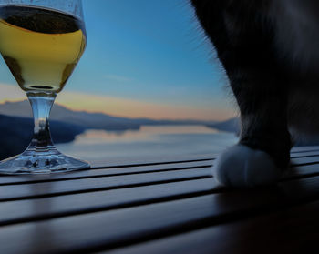 Close-up of beer glass on table against sea during sunset