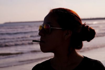 Close-up of silhouette woman smoking cigarette at beach during sunset