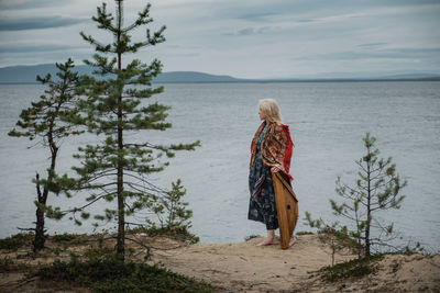 Rear view of woman standing at beach against sky