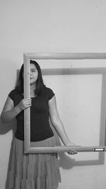 Portrait of woman holding frame while standing against wall