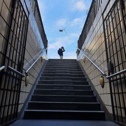 Low angle view of man on staircase amidst buildings against sky