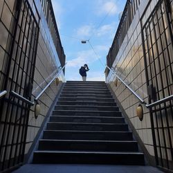 Low angle view of man using phone while standing against sky