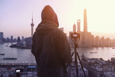 Rear view of person with tripod standing against cityscape during sunset