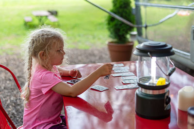 Little girl playing cards on a red outdoor table at a campsite