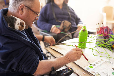 Mature disabled man painting twig at rehabilitation center