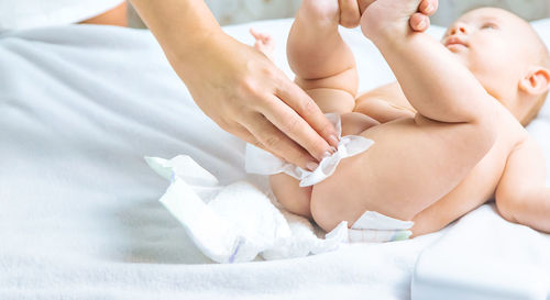 Mother cleaning baby lying on bed at home