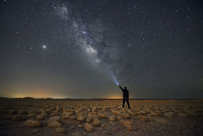 A man with a flashlight standing in the desert and the milky way